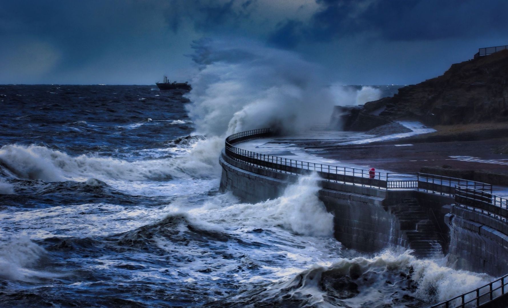 De fortes vagues frappent une digue côtière en béton sous un ciel sombre